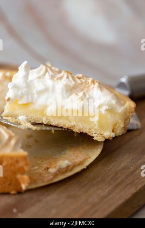 Lemon meringue sliced and being served with a cake slicer. On a wooden chopping board Stock Photo