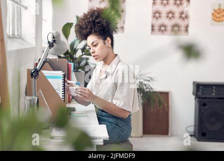 Young focused mixed race businesswoman making notes using sticky notes at work. One creative hispanic female businessperson with a curly afro planning Stock Photo