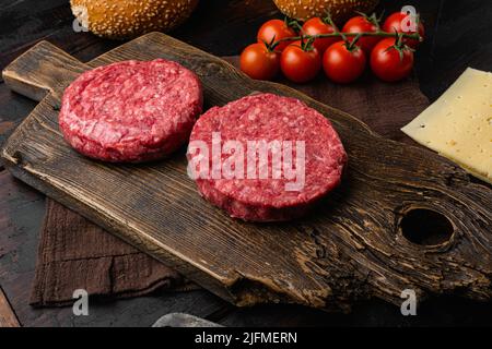 Raw fresh large beef burger on old dark wooden table background Stock Photo