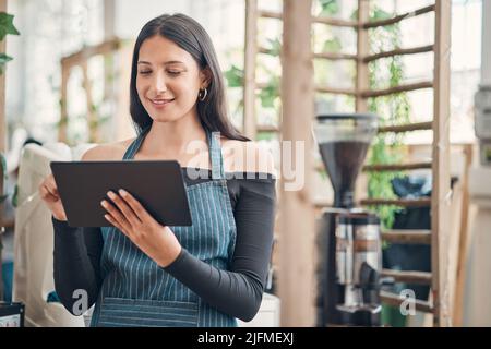 Shot of one young hispanic waitress using a digital tablet device while working in a store or cafe. Happy woman planning and browsing online while Stock Photo
