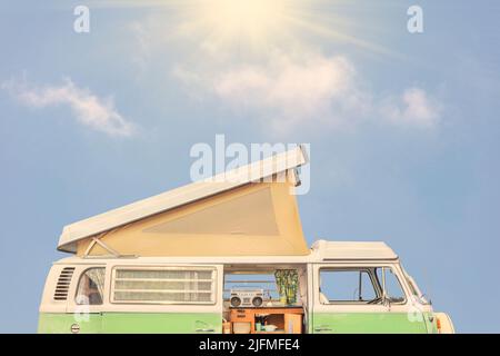 Side view of a seventies motor home in front of a blue sky with shining sun