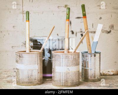 Retro styled image of used paint buckets and brushes in front of a stained wall Stock Photo