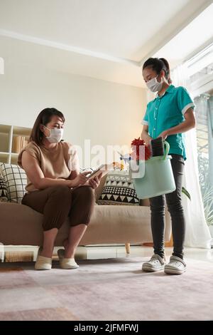 Woman in protective mask using digital tablet to leave feedback of cleaning service worker after her work Stock Photo