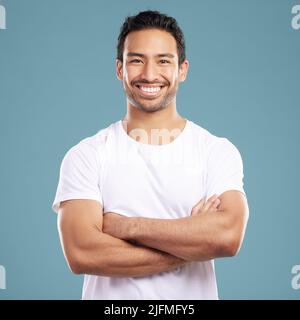 Handsome young mixed race man with his arms crossed while standing in studio isolated against a blue background. Happy hispanic male smiling while Stock Photo