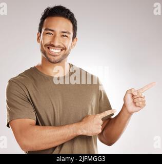 Handsome young mixed race man pointing towards copyspace while standing in studio isolated against a grey background. Happy hispanic male advertising Stock Photo