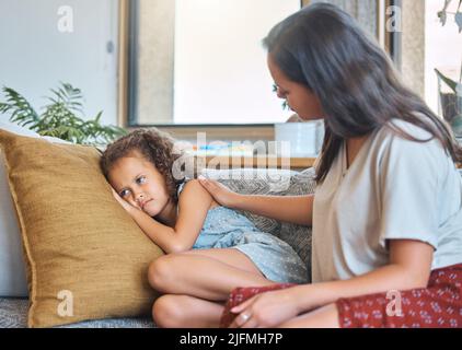 Sad depressed little girl lying on the couch and looking away while worried mother psychologist tries to talk to her. Loving caring mother trying to Stock Photo