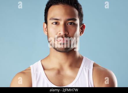 Handsome young hispanic man posing in studio isolated against a blue background. Mixed race male athlete wearing a vest and looking confident, healthy Stock Photo