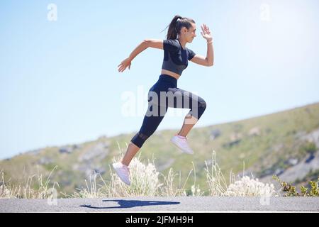 Young fit mixed race female running outside during a her daily exercise routine while jumping in mid air Stock Photo