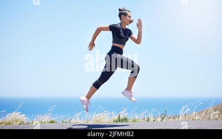 Young fit mixed race female running outside during a her daily exercise routine while jumping in mid air Stock Photo