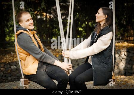 Young couple on a date sits on a swing in the forest among the trees Stock Photo