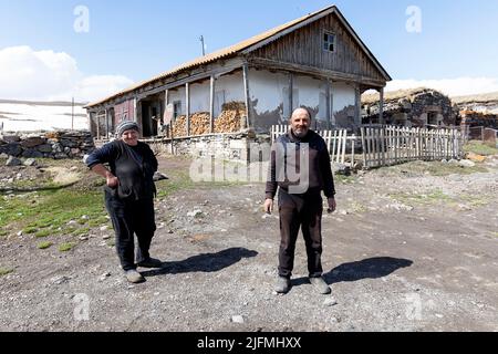 Man and woman standing in front of their beautiful unique turf-roofed traditional houses in Tambovka village at Lake Paravani, Javakheti, Georgia Stock Photo