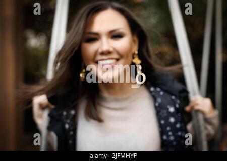 Blurred portrait of a young cheerful central asian woman swinging on a swing outdoor Stock Photo