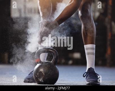 Closeup of unknown african american athlete using powder and chalk on hands before lifting kettlebell in gym. Strong, fit, active black man getting Stock Photo