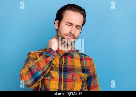 Photo of upset unhappy young man wear plaid shirt arm neck feeling tired isolated blue color background Stock Photo