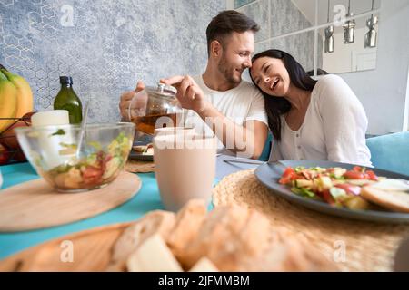 Laughing woman putting head on man shoulder during meal Stock Photo