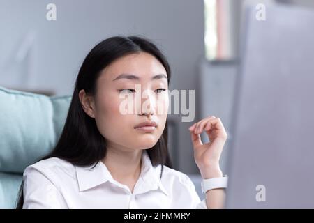 Close-up photo portrait of a young Asian woman office worker, wearing a white shirt, working in the office, looking at the monitor. Stock Photo