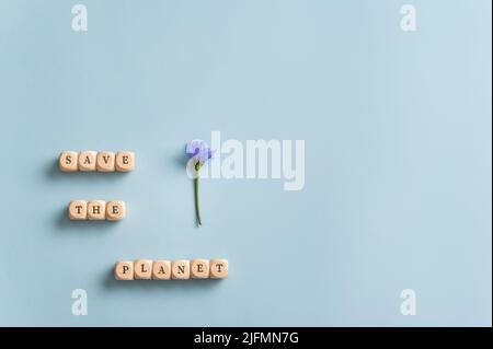 Save the planet sign spelled on wooden dice next to a delicate purple flower on blue background. Stock Photo