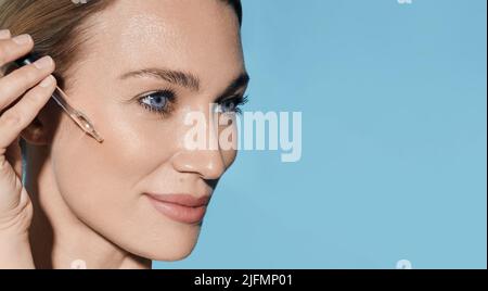 Beautiful woman applying essential oil on her face for hydrated skin using pipette dropper. facial skin care with treatment essential oil and serum Stock Photo