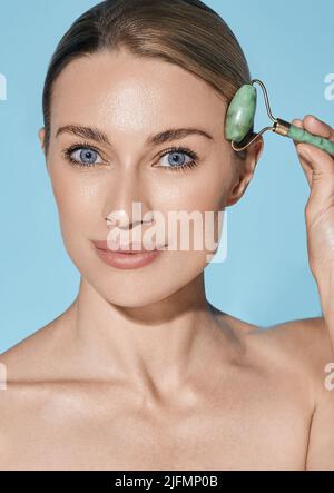 Portrait of adult woman using jade roller or stone roller for facial lifting procedure Stock Photo