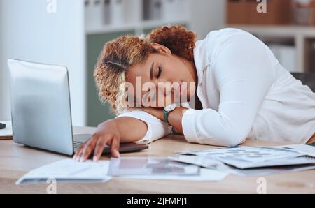 Young mixed race businesswoman sleeping at her desk in an office alone at work. Hispanic woman taking a nap while working with a laptop. Female boss Stock Photo