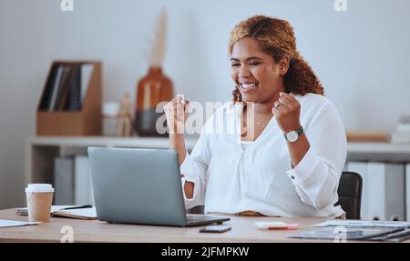 Happy and cheerful mixed race business woman cheering while working on a laptop in office. Confident hispanic female boss smiling while celebrating a Stock Photo