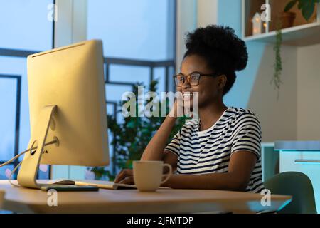 Pleased smiling young black female remote worker web designer or graphics editor at cozy home office Stock Photo