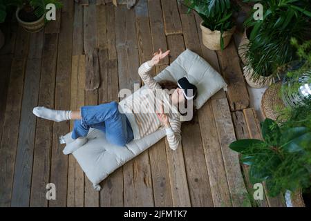 Young astonished woman in casual clothes feeling excited while using 360 VR headset at home Stock Photo
