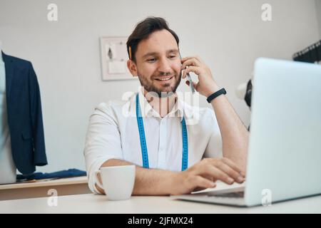 Man couturier talking on phone looking at laptop screen Stock Photo