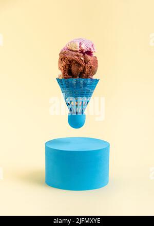 Badminton shuttlecock filled with scoops of ice cream above a blue roller on a yellow background. Minimal abstract summer concept. Rectangle layout wi Stock Photo