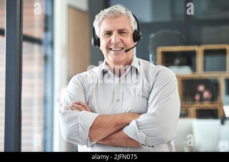 Im ready to make a difference. Shot of a mature call centre agent standing alone in the office with his arms folded. Stock Photo