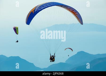 Paragliding in the sky. Paraglider tandem flying over the sea with mountains at sunset. Aerial view of paraglider and Blue Lagoon in Oludeniz, Mugla, Stock Photo