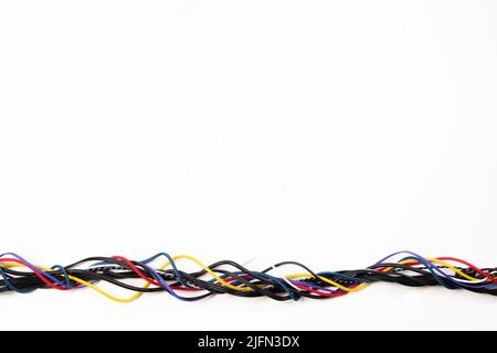 Many colorful electrical cord cables twist together into single frame line on white background. Top view, copy space Stock Photo
