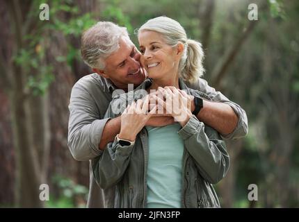 A senior caucasian couple smiling and looking happy in a forest during a hike in the outdoors. Man and wife showing affection and holding each other Stock Photo