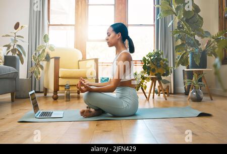 Its all about comfort. Shot of a sporty young woman meditating while using a laptop at home. Stock Photo