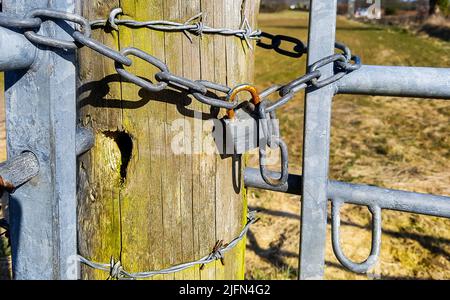 two galvanised steel farm gates chained together by rusting padlock via a substantial round wooden post with barbed wired wrapped around it Stock Photo