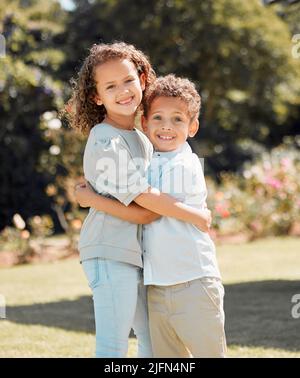Portrait of a mixed race brother and sister smiling, standing and embracing each other in a garden outside. Hispanic Male and female siblings showing Stock Photo