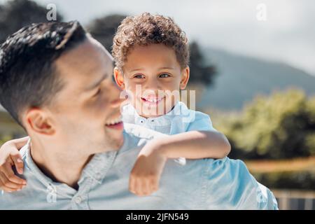 Father carrying boy on back while spending time together outdoors on a sunny day. Adorable mixed race kid having fun playing with dad and getting a