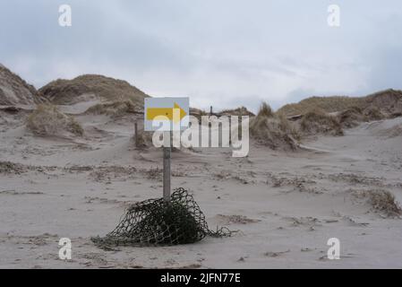 direction sign, yellow arrow on white ground, placed on a beach with sand dunes in the back Stock Photo