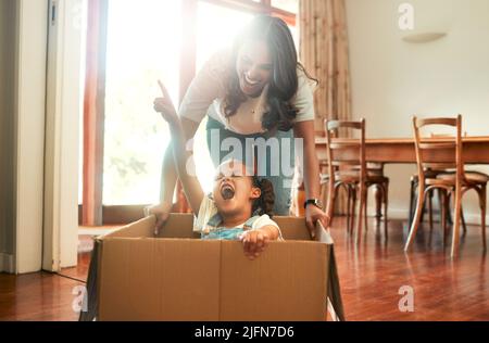 Mother and daughter playing with a cardboard box. Excited little girl sitting in a box. Parent pushing her daughter in a box. Parent having fun with Stock Photo
