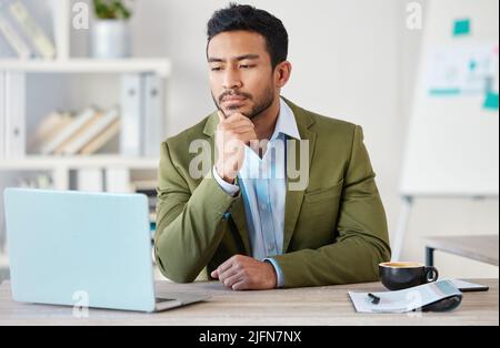 Young focused mixed race businessman working alone on a laptop in an office at work. One hispanic male boss thinking while reading an email on a Stock Photo