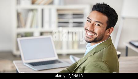 Portrait of one confident young mixed race businessman working on laptop at desk in an office. Ambitious motivated entrepreneur and leader dedicated Stock Photo