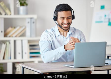 Closeup of smiling mixed race call centre agent smiling while wearing headset. Young male customer service representative using wireless headset and Stock Photo