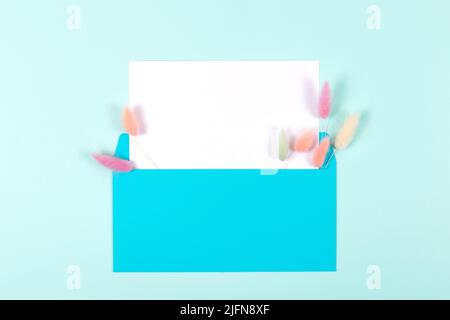 Blue envelope with blank card decorated with colourful fluffy spikelets on pastel blue background. Flat lay style. Greeting concept Stock Photo