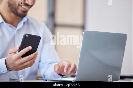 Closeup of business man using smartphone and laptop in office. Man using mobile phone app for synchronizing data with laptop. Getting confirmation Stock Photo