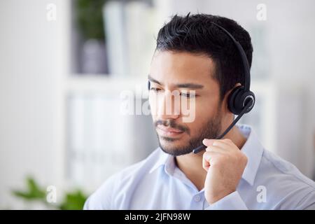 A mixed race man working in a call center. Operator using a wireless headset, consulting online or making a call. A male customer support agent Stock Photo