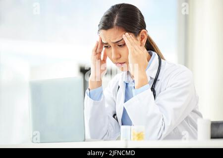 Closeup of a young mixed race doctor looking worried and suffering from a headache while working on a computer in her office. Hispanic female Stock Photo