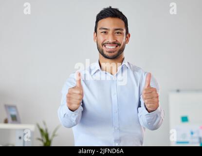 Smiling businessman showing thumbs up sign with copyspace. Portrait of asian professional standing alone and using hand gesture to symbol good luck Stock Photo