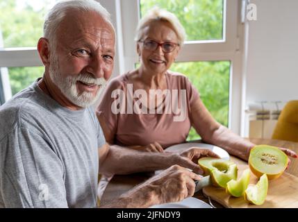 Senior couple sitting at dining table at home and eating melon in summer time Stock Photo
