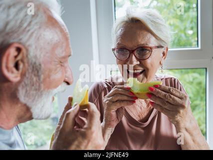 Senior couple sitting at dining table at home and eating melon in summer time Stock Photo