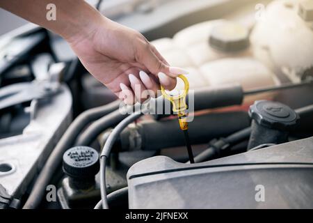 Woman checking her car oil. Woman repairing her car engine. Mechanic looking for a vehicle problem. Closeup of hand of woman using a dipstick to check Stock Photo
